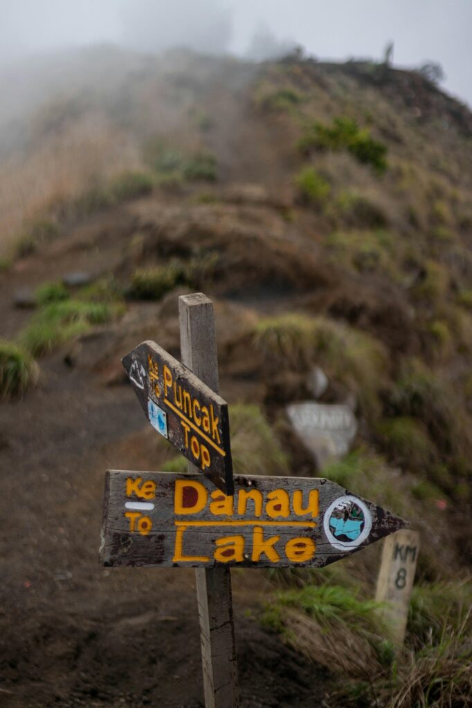 Trekking trail sign showing direction to Mount Rinjani summit and Segara Anak lake in Lombok.