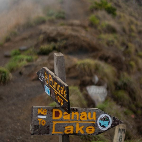 Trekking trail sign showing direction to Mount Rinjani summit and Segara Anak lake in Lombok.